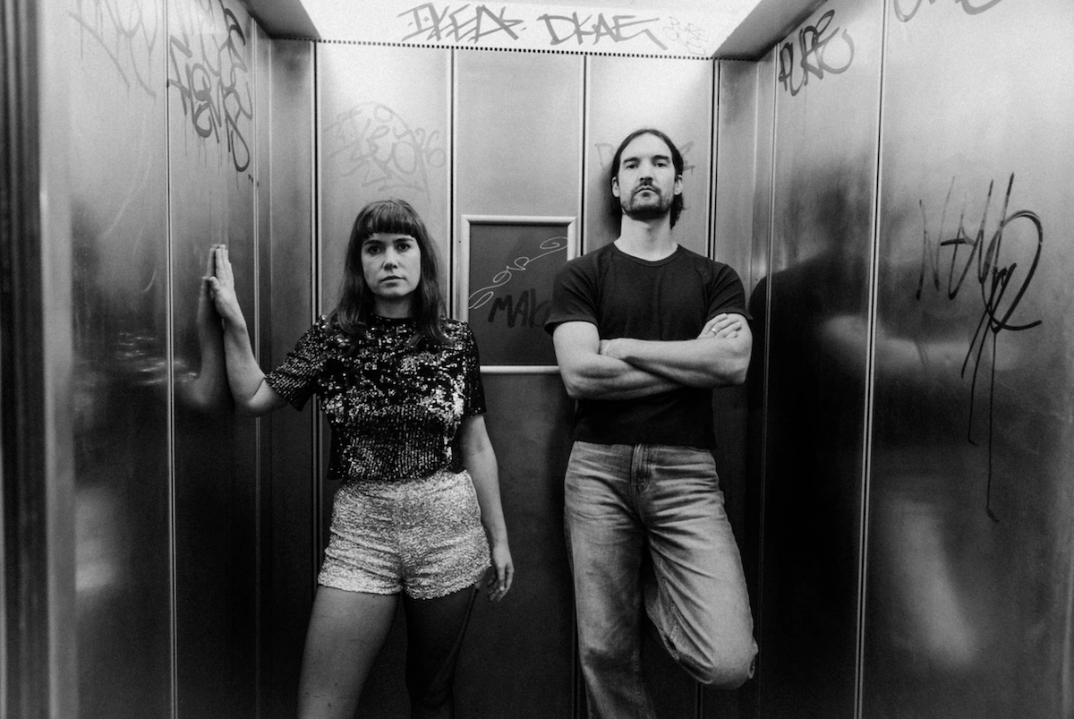 Black and white promo portrait of musical duo Party Dozen posing inside a graffiti-tagged elevator.